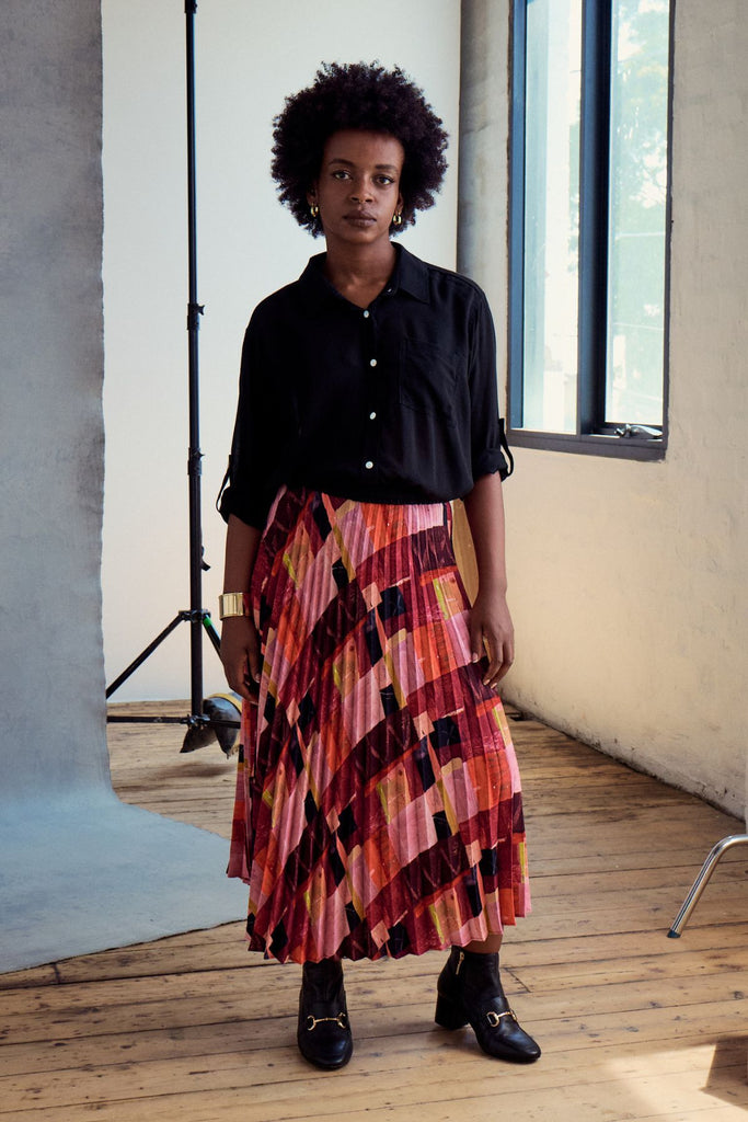 Olga de Polga classic pleated skirt in printed Kismet Blush Pink. Midi length. Fully elasticated waistband. Front view on model worn with a black shirt.