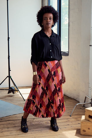 Olga de Polga classic pleated skirt in printed Kismet Blush Pink. Midi length. Fully elasticated waistband.  Side front view on model with black shirt.