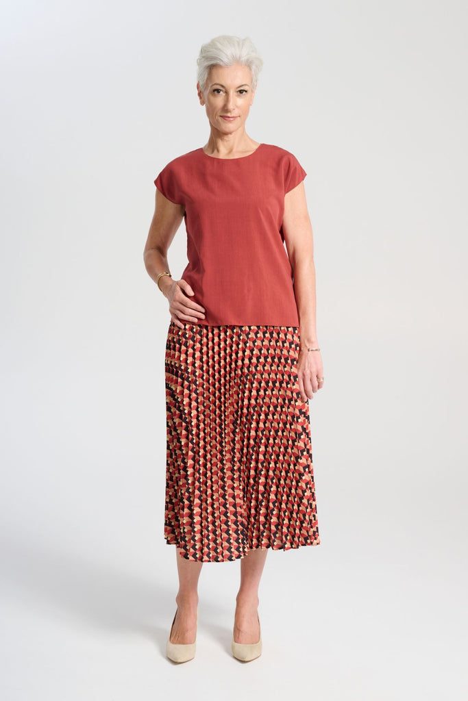 Olga de Polga printed pleat skirt in the Seraph Sunset print. Shades of orange, red and black. Fully elasticated waistband.   Front view modelled with a tee in dark blush coral colour.