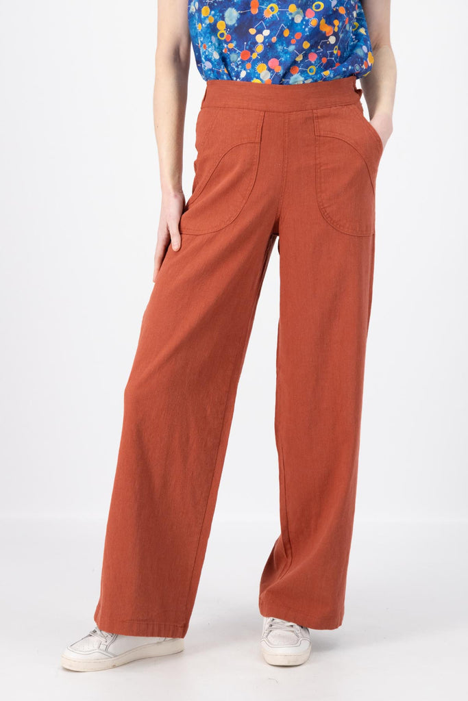 Olga de Polga Peggy Pants Long Lino in Rose Brick linen. Featuring a flattering high waist with an elasticated back, these pants provide all-day comfort while maintaining a sleek, streamlined look. With their stretchy wide-leg fit, flat front, and full-length silhouette, they effortlessly elevate any outfit. Front close-up view on model.