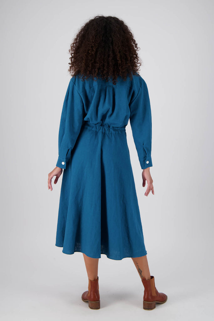 Olga de Polga Teal Parisian Estate dress in 100% Linen. Straight silhouette with a cinched waistband. Two buttons on the front allow the waistband to be adjusted. Elastic waistband at the back.  Back full view on model