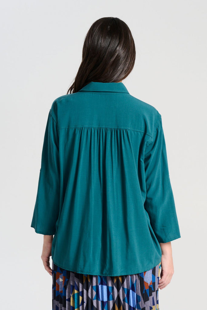 Olga de Polga Teal Rhea shirt in 100% soft Tencel. The front of the shirt sits at the waist while the back falls to the hips for a lovely drape. Perfect for leaving loose over pants or for tucking into any bottoms. Back view on model