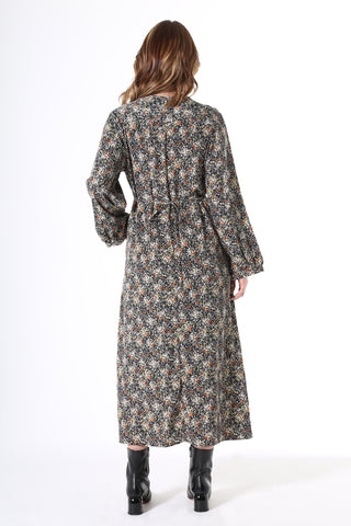 Olga de Polga Botanical Tie Dress. Featuring soft pleats on the bustline, gathers under the waist, balloon sleeves with a buttoned cuff and oversized drape pockets. The waist tie is concealed at the front then wraps around to be visible at the back - to draw in the waist. Botanical print with a navy background with beige, grey yellow & orange flowers in a smooth mid-weight fluid viscose.