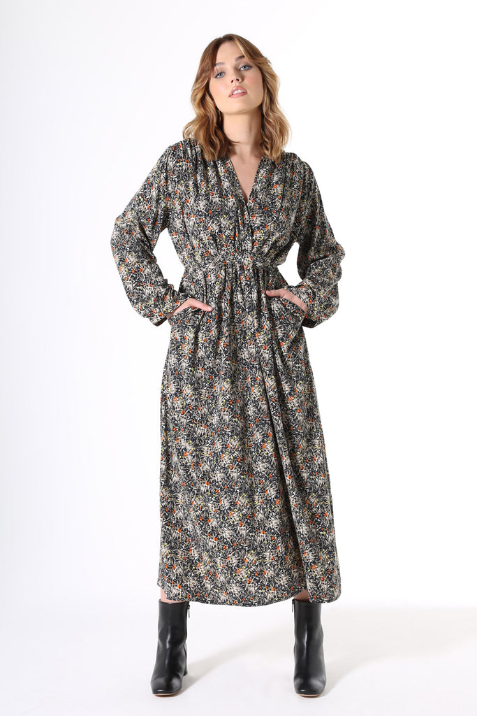 Olga de Polga Botanical Tie Dress. Featuring soft pleats on the bustline, gathers under the waist, balloon sleeves with a buttoned cuff and oversized drape pockets. The waist tie is concealed at the front then wraps around to be visible at the back - to draw in the waist. Botanical print with a navy background with beige, grey yellow & orange flowers in a smooth mid-weight fluid viscose. 