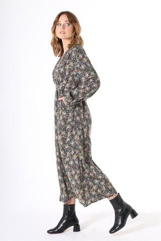 Olga de Polga Botanical Tie Dress. Featuring soft pleats on the bustline, gathers under the waist, balloon sleeves with a buttoned cuff and oversized drape pockets. The waist tie is concealed at the front then wraps around to be visible at the back - to draw in the waist. Botanical print with a navy background with beige, grey yellow & orange flowers in a smooth mid-weight fluid viscose.