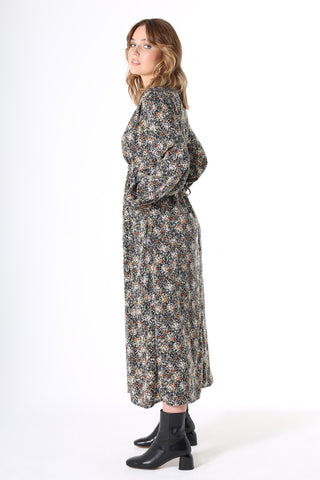 Olga de Polga Botanical Tie Dress. Featuring soft pleats on the bustline, gathers under the waist, balloon sleeves with a buttoned cuff and oversized drape pockets. The waist tie is concealed at the front then wraps around to be visible at the back - to draw in the waist. Botanical print with a navy background with beige, grey yellow & orange flowers in a smooth mid-weight fluid viscose.