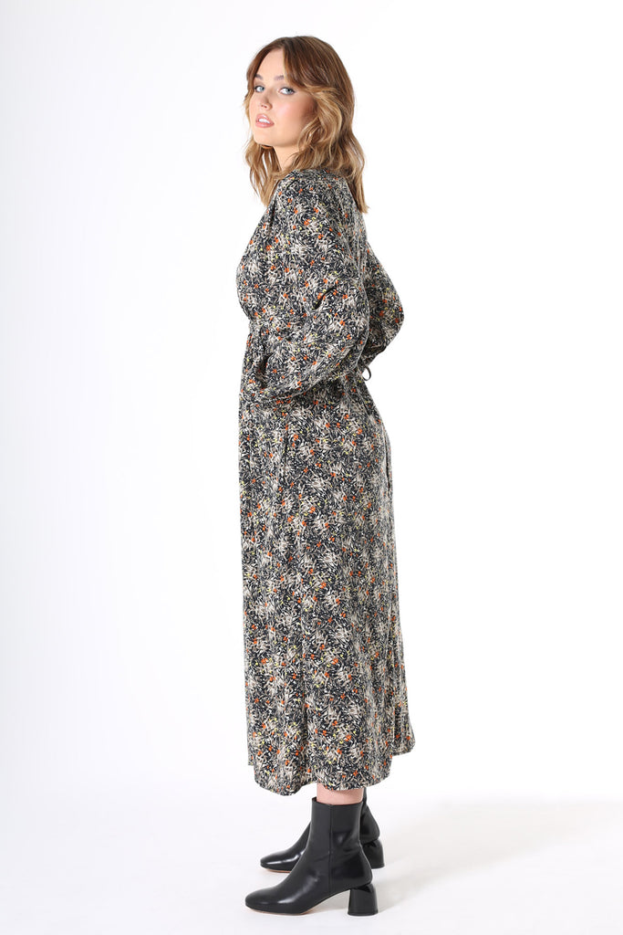 Olga de Polga Botanical Tie Dress. Featuring soft pleats on the bustline, gathers under the waist, balloon sleeves with a buttoned cuff and oversized drape pockets. The waist tie is concealed at the front then wraps around to be visible at the back - to draw in the waist. Botanical print with a navy background with beige, grey yellow & orange flowers in a smooth mid-weight fluid viscose.