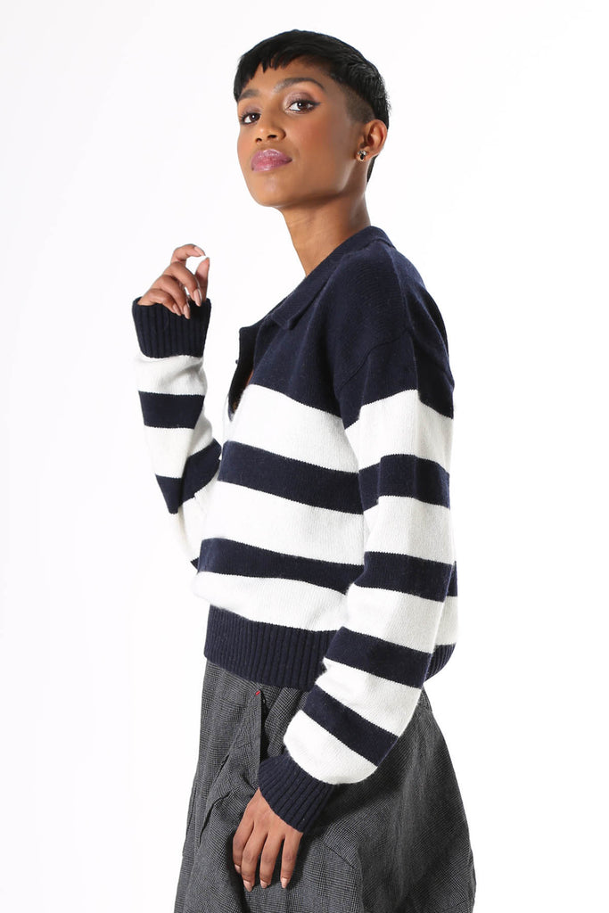 Olga de Polga knitwear. Seoul short sweater in navy and white stripes. Cropped length, relaxed fit, with an open collar, v-neck and dropped shoulder.  Side view on Model