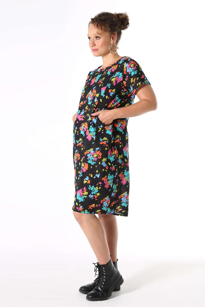 Olga de Polga knee length shift dress with short sleeves and pockets. Printed in Deep black with splashes of neon pink, orange, yellow and aqua. Soft, light-weight cotton/rayon fabric with a floaty drape.  